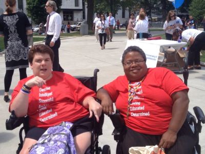 2 women in wheelchairs wearing advocacy shirts. They are smiling
